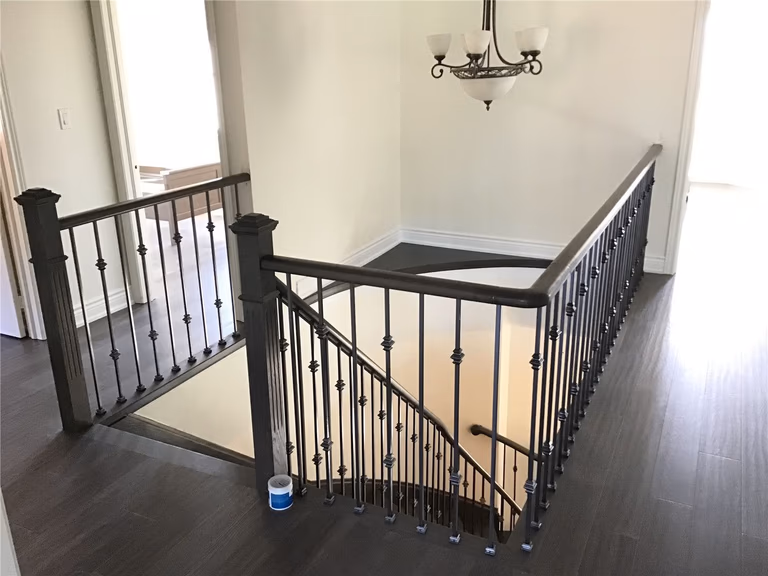 This Woodbridge interior renovation showcases a modern staircase upgrade featuring custom iron railings paired with dark hardwood flooring. The design enhances both safety and visual appeal, creating a clean and elegant transition between floors.
