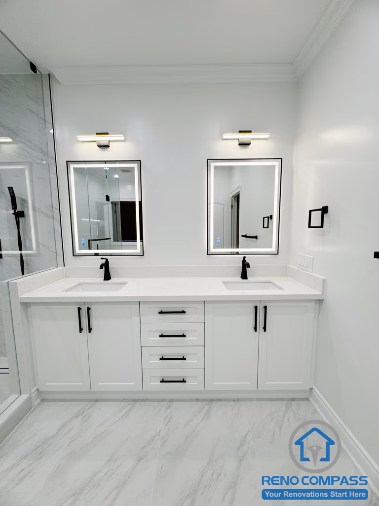 This Vaughan bathroom renovation showcases a custom double vanity with a quartz countertop, integrated drawers, and matte black fixtures. Two modern mirrors with wall-mounted lighting provide balanced illumination, enhancing both functionality and visual symmetry. Finished with marble-look flooring and clean white cabinetry, this space was completed by a professional Toronto Renovation Company with a focus on durability, storage efficiency, and timeless modern design.