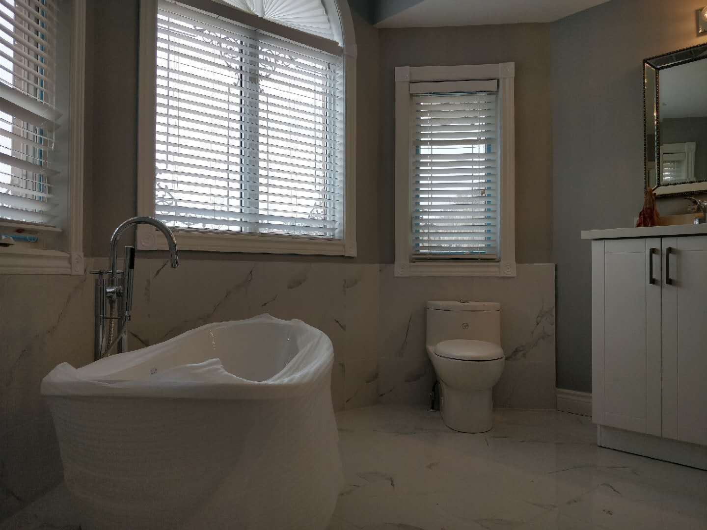 This bathroom renovation in Ajax features a freestanding bathtub, modern vanity, and elegant tile finishes, creating a bright and relaxing space. Large windows bring in natural light, enhancing the overall comfort and spa-like atmosphere. As part of a full home renovation, this bathroom upgrade combines functionality with a clean and luxurious design.