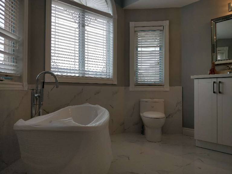 This bathroom renovation in Ajax features a freestanding bathtub, modern vanity, and elegant tile finishes, creating a bright and relaxing space. Large windows bring in natural light, enhancing the overall comfort and spa-like atmosphere. As part of a full home renovation, this bathroom upgrade combines functionality with a clean and luxurious design.