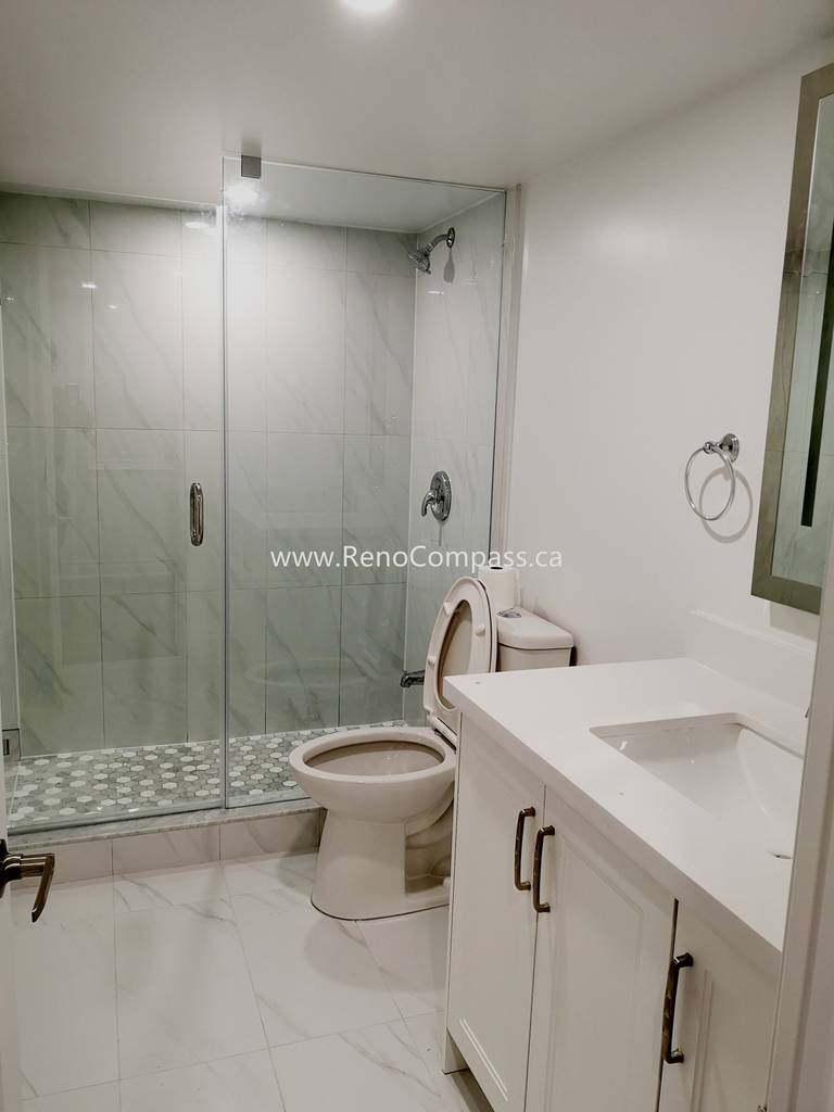 This Vaughan basement bathroom renovation showcases a modern glass shower enclosure with elegant marble-style wall tiles and a clean, minimalist layout. The upgraded space includes a sleek vanity, contemporary fixtures, and durable floor tiles designed for both style and functionality. Completed by Reno Compass Inc., this basement bathroom upgrade enhances comfort, increases home value, and creates a bright, modern space that complements the fully renovated basement.