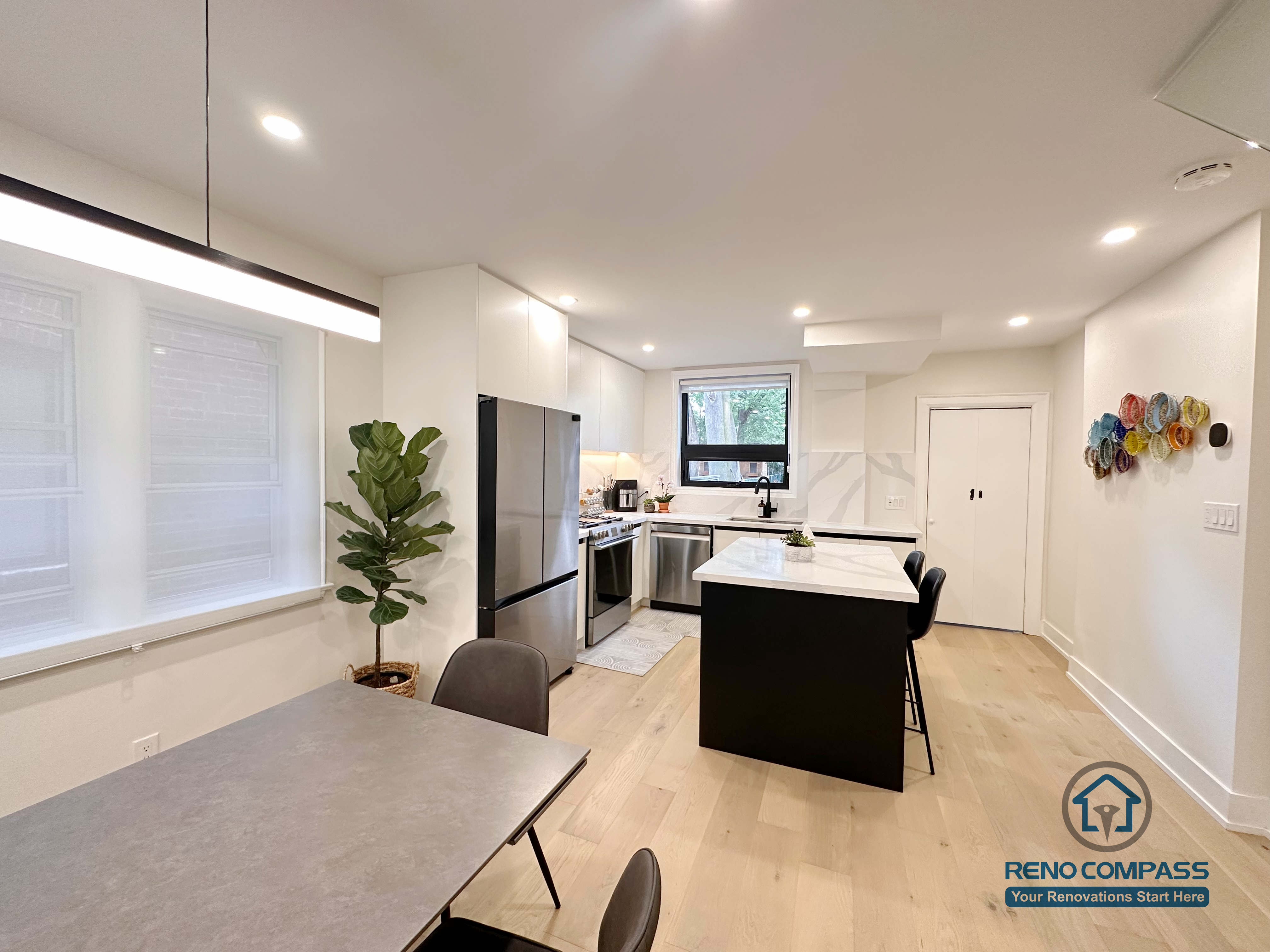This Toronto interior renovation features a cohesive kitchen and dining area with a central island, quartz countertops, flat-panel cabinetry, stainless steel appliances, and warm wide-plank hardwood flooring. The open layout enhances everyday functionality and visual balance, showcasing thoughtful design and execution by a trusted Toronto renovation company.