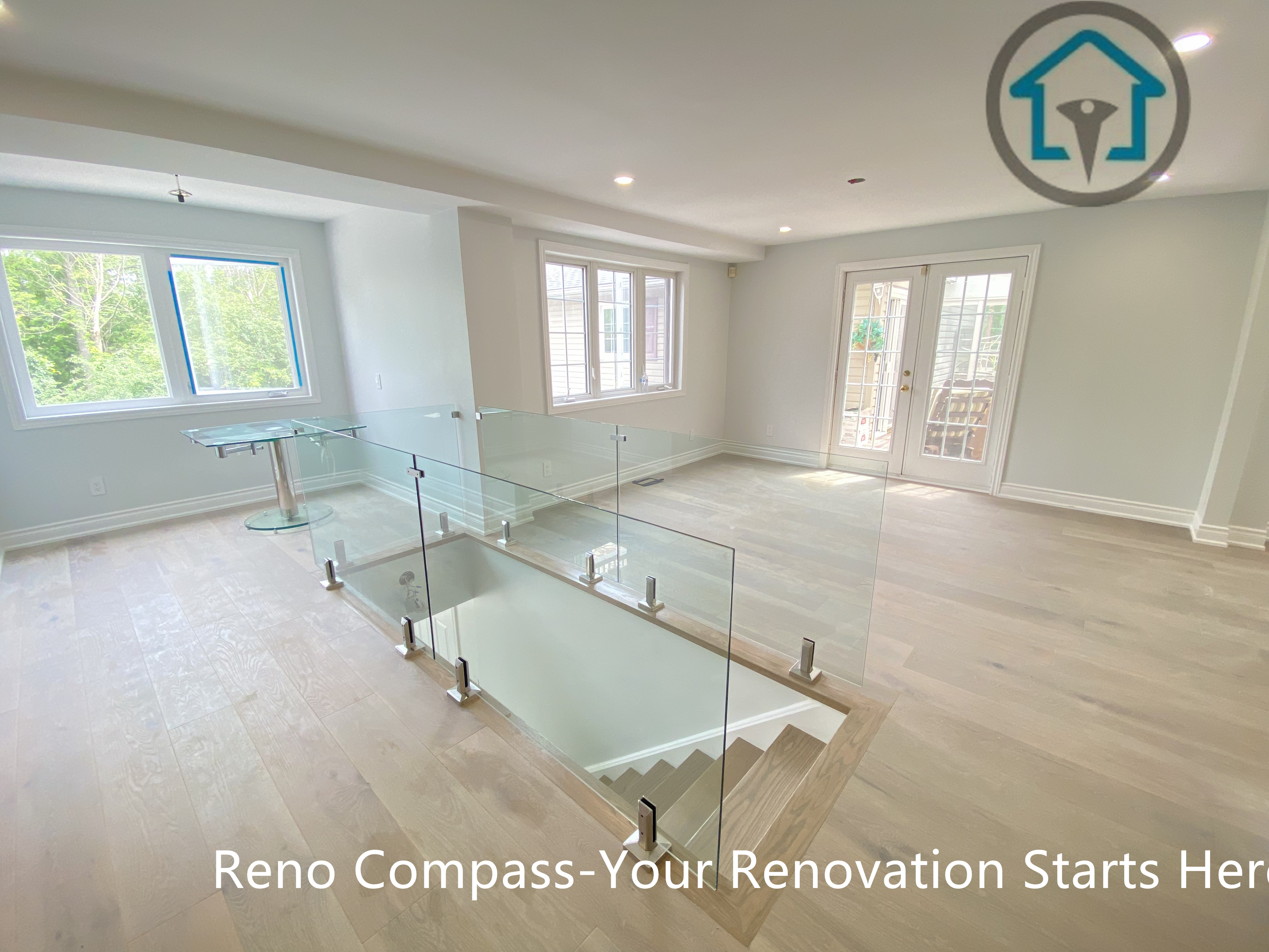 This upper-level living area features wide-plank flooring, a full glass railing overlooking the staircase, and large windows that bring in abundant natural light. The open layout enhances spatial flow while maintaining a bright, airy atmosphere, making the space ideal for flexible living or family use.