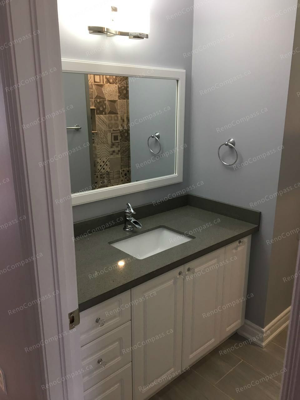 This Markham interior renovation highlights a modern bathroom vanity upgrade featuring white cabinetry, a sleek quartz countertop, and a framed wall mirror with contemporary lighting. Neutral wall tones and durable floor tiles create a clean and cohesive finish. Completed by a reliable Toronto renovation company, this bathroom renovation enhances storage, functionality, and everyday comfort with refined detailing.