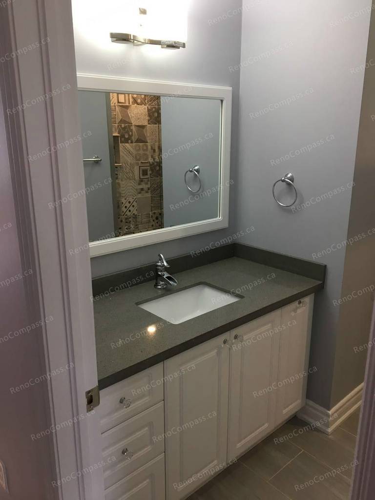 This Markham interior renovation highlights a modern bathroom vanity upgrade featuring white cabinetry, a sleek quartz countertop, and a framed wall mirror with contemporary lighting. Neutral wall tones and durable floor tiles create a clean and cohesive finish. Completed by a reliable Toronto renovation company, this bathroom renovation enhances storage, functionality, and everyday comfort with refined detailing.