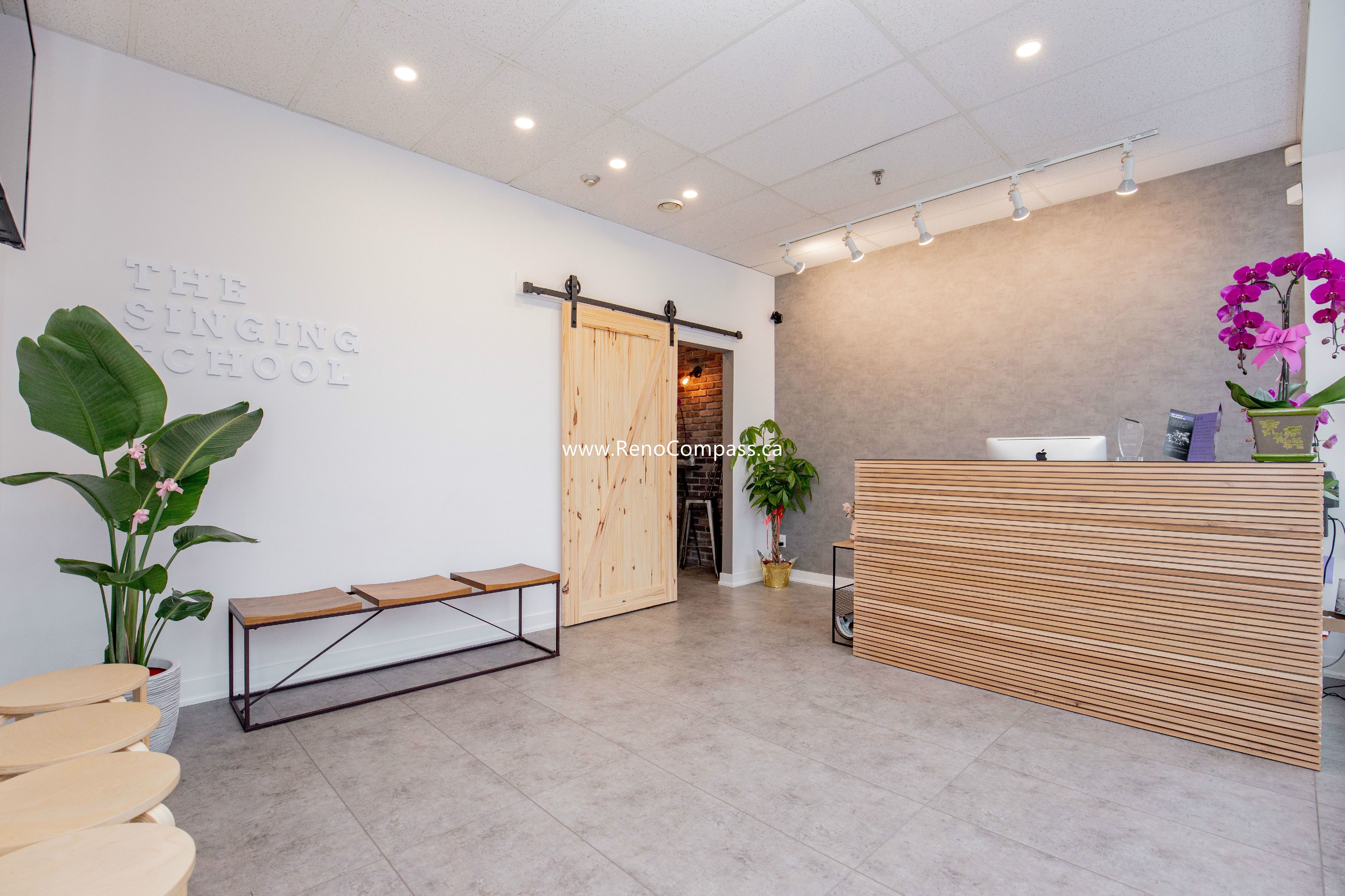 A stunning lobby renovation for The Singing School in Richmond Hill featuring a custom slatted wood reception desk, industrial barn door, and sleek large-format floor tiles. This professional commercial build-out highlights modern interior design and high-end finishes.