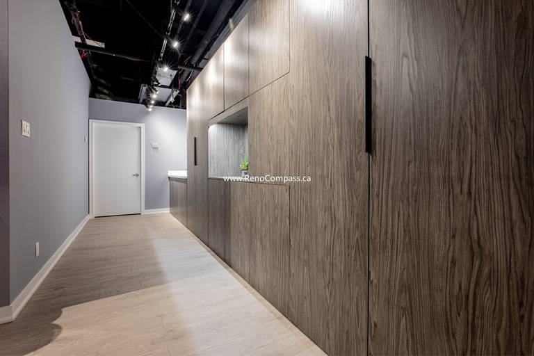 High-end custom wood cabinetry and integrated millwork for a commercial hallway. Features modern track lighting, exposed black ceilings, and luxury vinyl flooring. A professional interior renovation project by RenoCompass in Richmond Hill.