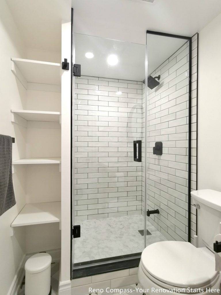 This image showcases a walk-in shower area from a completed basement renovation in Vaughan, featuring classic white subway tile walls, a frameless glass enclosure, and matte black shower fixtures. Built-in open shelving provides practical storage for everyday use, helping maintain a clean and organized bathroom layout. The combination of moisture-resistant materials, precise tile installation, and efficient space planning enhances both durability and functionality. This basement bathroom renovation reflects the attention to detail and craftsmanship delivered by a professional Toronto renovation company specializing in high-quality basement upgrades.