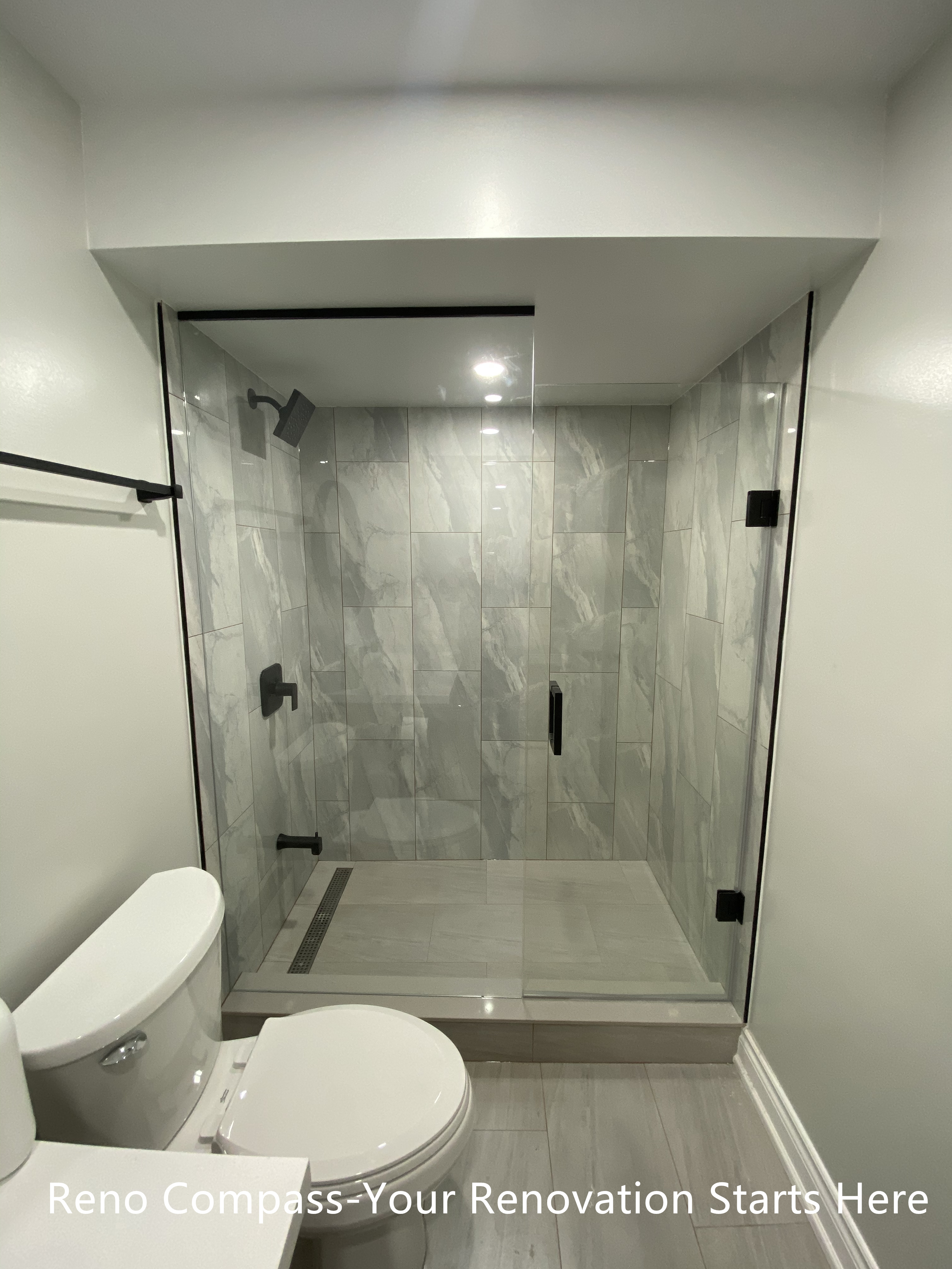 This Aurora basement bathroom renovation features a clean and modern walk-in shower design with full-height porcelain tile and a frameless glass enclosure. The layout is carefully planned to work within basement ceiling constraints while maintaining a bright, open feel. Matte black fixtures add a contemporary contrast against the neutral tile palette, and the linear floor drain improves both function and drainage efficiency. The result is a practical, low-maintenance bathroom designed for everyday use. Completed by Reno Compass, a Toronto renovation contractor specializing in basement renovations.
