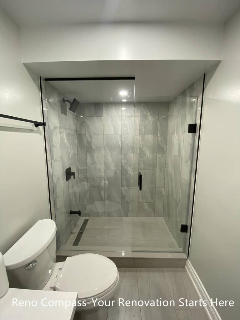 This Aurora basement bathroom renovation features a clean and modern walk-in shower design with full-height porcelain tile and a frameless glass enclosure. The layout is carefully planned to work within basement ceiling constraints while maintaining a bright, open feel. Matte black fixtures add a contemporary contrast against the neutral tile palette, and the linear floor drain improves both function and drainage efficiency. The result is a practical, low-maintenance bathroom designed for everyday use. Completed by Reno Compass, a Toronto renovation contractor specializing in basement renovations.