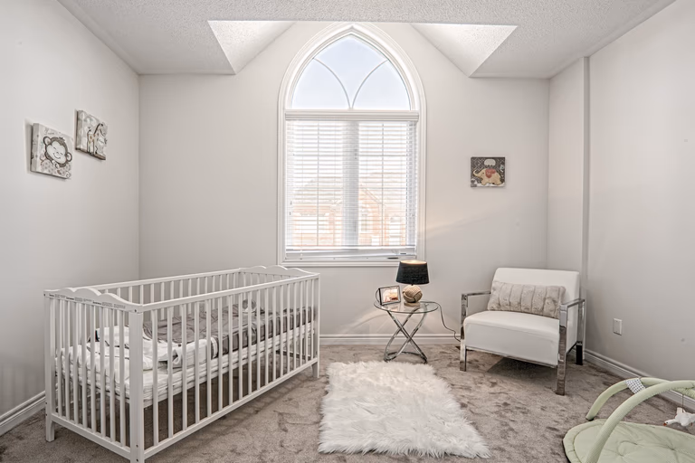 This Toronto nursery room renovation features a bright and cozy kids bedroom with a high ceiling and elegant arched window that fills the space with natural light. The design includes soft neutral tones, premium carpeting, and a functional layout that creates a warm and comfortable environment for a growing family. Completed by a professional Toronto renovation company, this residential interior project highlights thoughtful space planning, modern finishes, and family-friendly design for contemporary living.