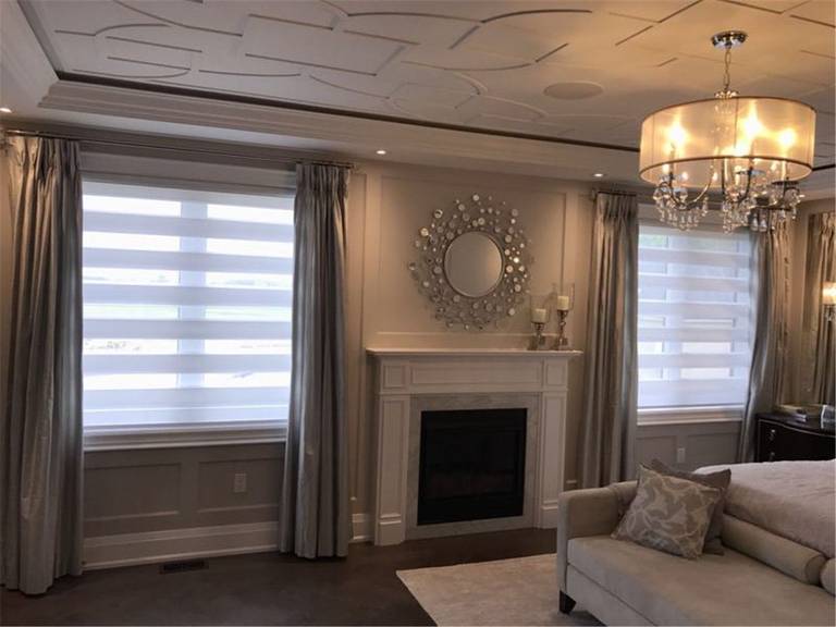 Modern living room in Toronto featuring layered window treatment with zebra blinds and full-length curtains. This combination provides flexible light control, privacy, and a clean, elegant finish that complements the fireplace and custom ceiling design.