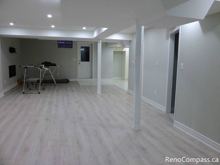 Spacious open-concept basement renovation in Markham featuring light-toned laminate flooring, recessed pot lights, structural support columns, and a clean neutral color palette. This professionally finished basement creates a bright and versatile living area ideal for entertainment, gym space, or family use. Completed by a reliable Toronto renovation company, this project showcases functional design and quality basement finishing craftsmanship.
