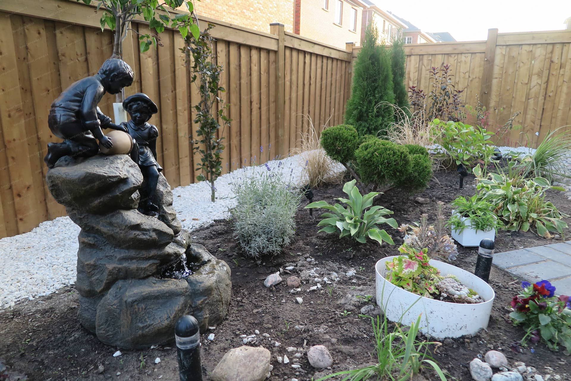 Front yard landscaping renovation in Vaughan featuring a decorative stone pathway, river rock garden bed, ornamental shrubs, and layered plant design. This garden layout enhances the entrance walkway while creating a natural transition between the driveway, lawn, and front yard landscape.