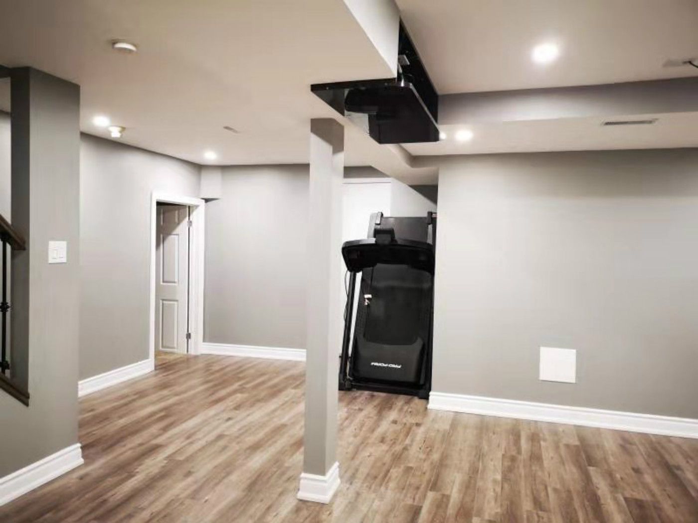 This finished basement renovation in Mississauga features durable vinyl flooring, recessed pot lights, and a clean open-concept layout with structural columns. The space is designed for multi-functional use, including a home gym area, showcasing the expertise of a professional Toronto renovation company in delivering modern, practical basement transformations.