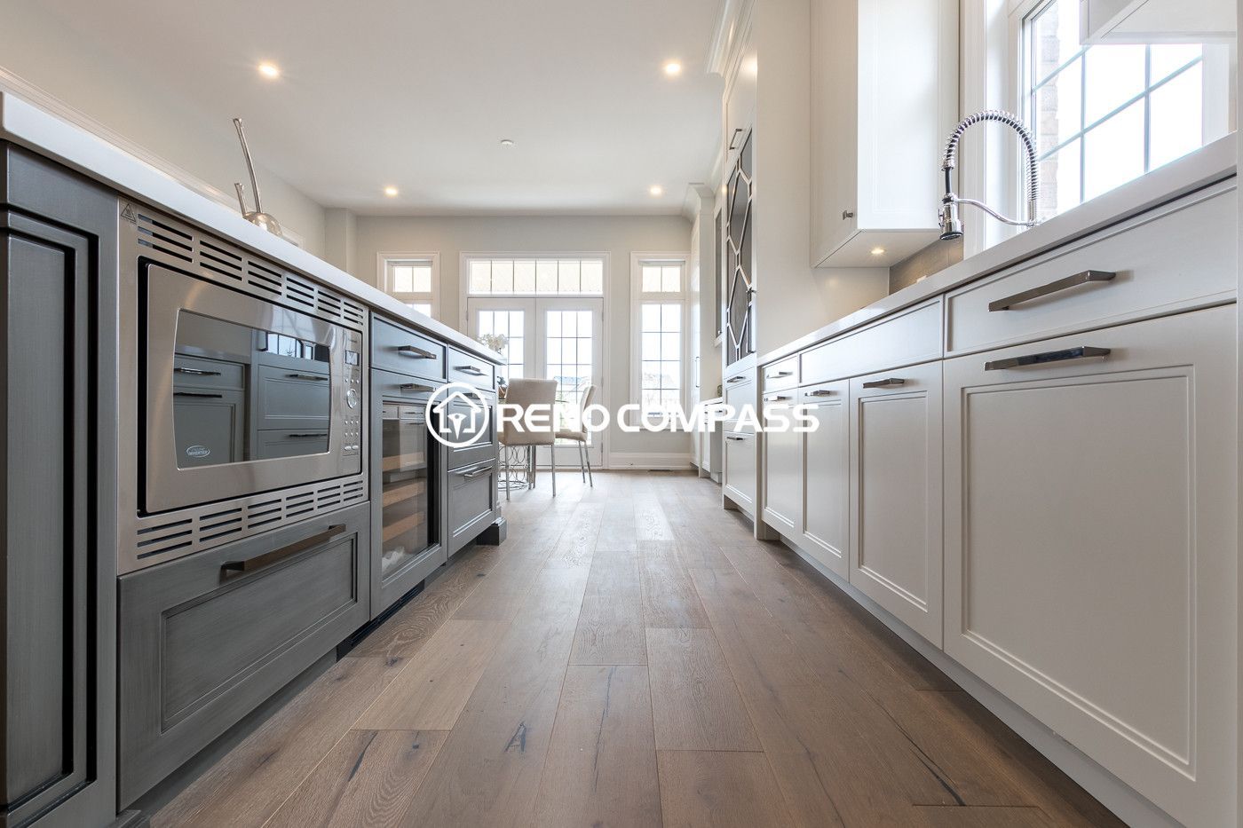 Beautiful kitchen renovation in Newmarket showcasing a large island with built-in appliances, custom white cabinetry, modern faucet and sink, and engineered hardwood flooring. The open layout connects the kitchen seamlessly with the dining and living area, creating a bright and functional family space.