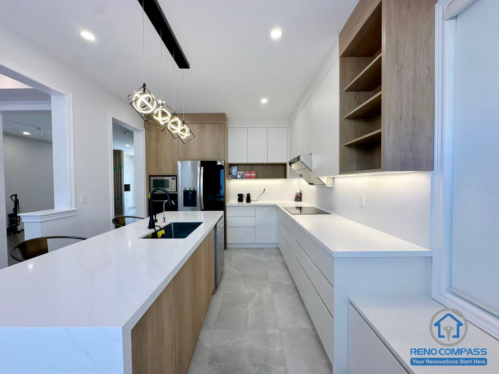 This Stouffville kitchen renovation features a long custom island with integrated sink, white quartz countertops, and a combination of wood-tone and matte white cabinetry. Recessed lighting and modern pendant fixtures enhance brightness and depth throughout the space. Designed and built by a trusted Toronto renovation company, Reno Compass Inc., this project highlights efficient workflow, clean lines, and contemporary interior craftsmanship.