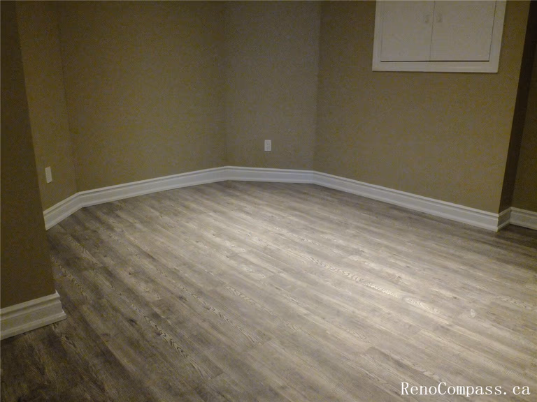 View of a finished basement room in this Ajax basement renovation, featuring durable vinyl plank flooring, neutral wall tones, and recessed pot lights for bright, even lighting. The clean layout and modern finishes make this space ideal for a home office, guest room, or recreation area. Completed by a professional Toronto Renovation Company, the renovation focuses on comfort, functionality, and long-lasting materials suitable for basement living spaces.