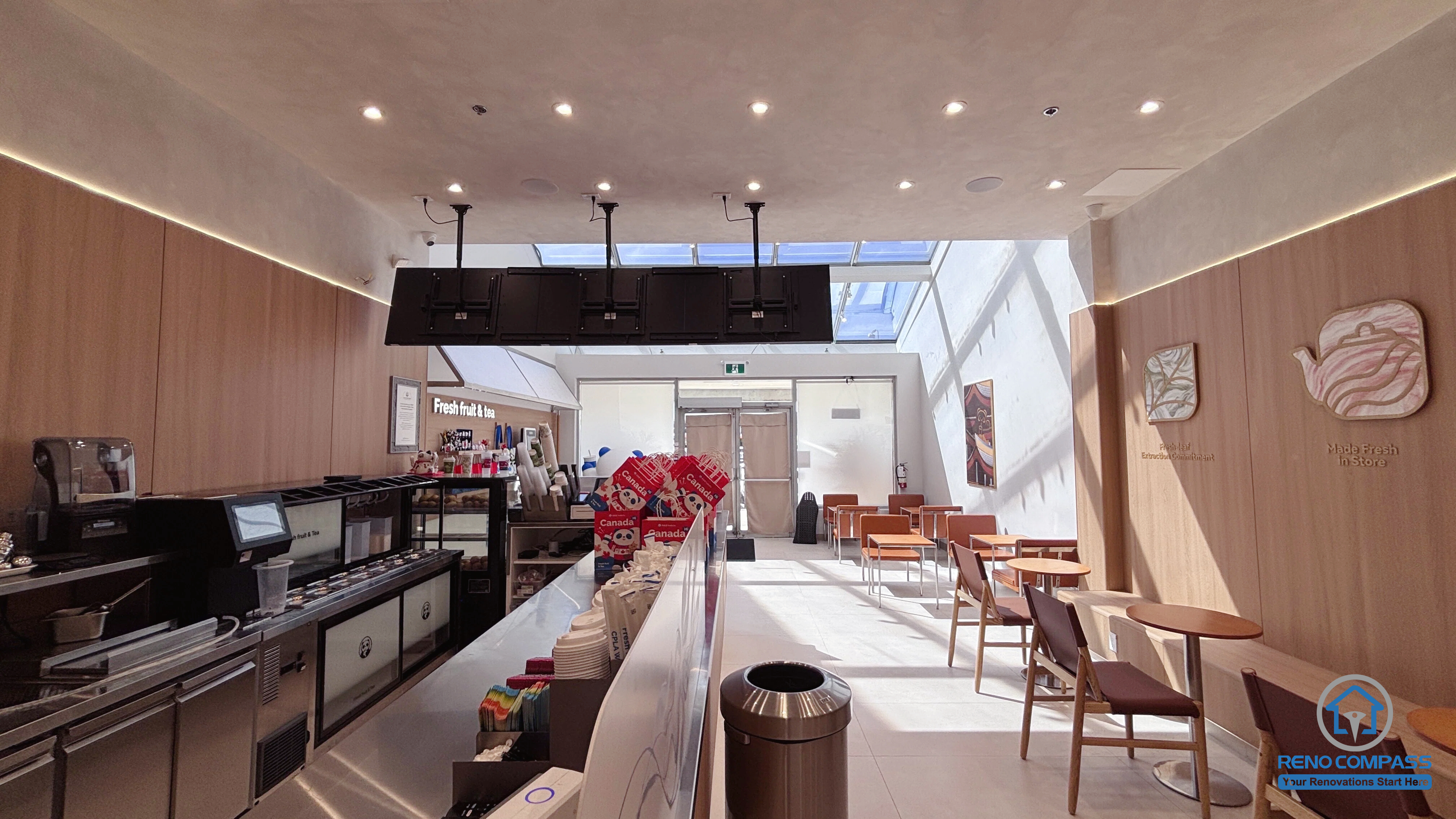 Completed TEABYDO bubble tea shop renovation in Richmond Hill featuring an open-concept beverage preparation counter, modern café seating area, skylight ceiling, custom wood-tone commercial millwork, integrated LED lighting, and clean minimalist interior design. This commercial renovation project was completed by Reno Compass serving Richmond Hill, Toronto, and the GTA.