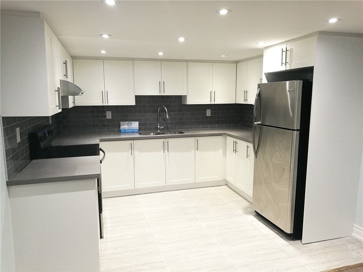 Modern kitchen interior renovation project in Pickering featuring white flat-panel cabinetry, dark subway tile backsplash, stainless steel appliances, and recessed pot lighting. This clean and functional kitchen design enhances storage, lighting, and everyday usability, serving as a reference for Toronto renovation company kitchen remodeling projects.