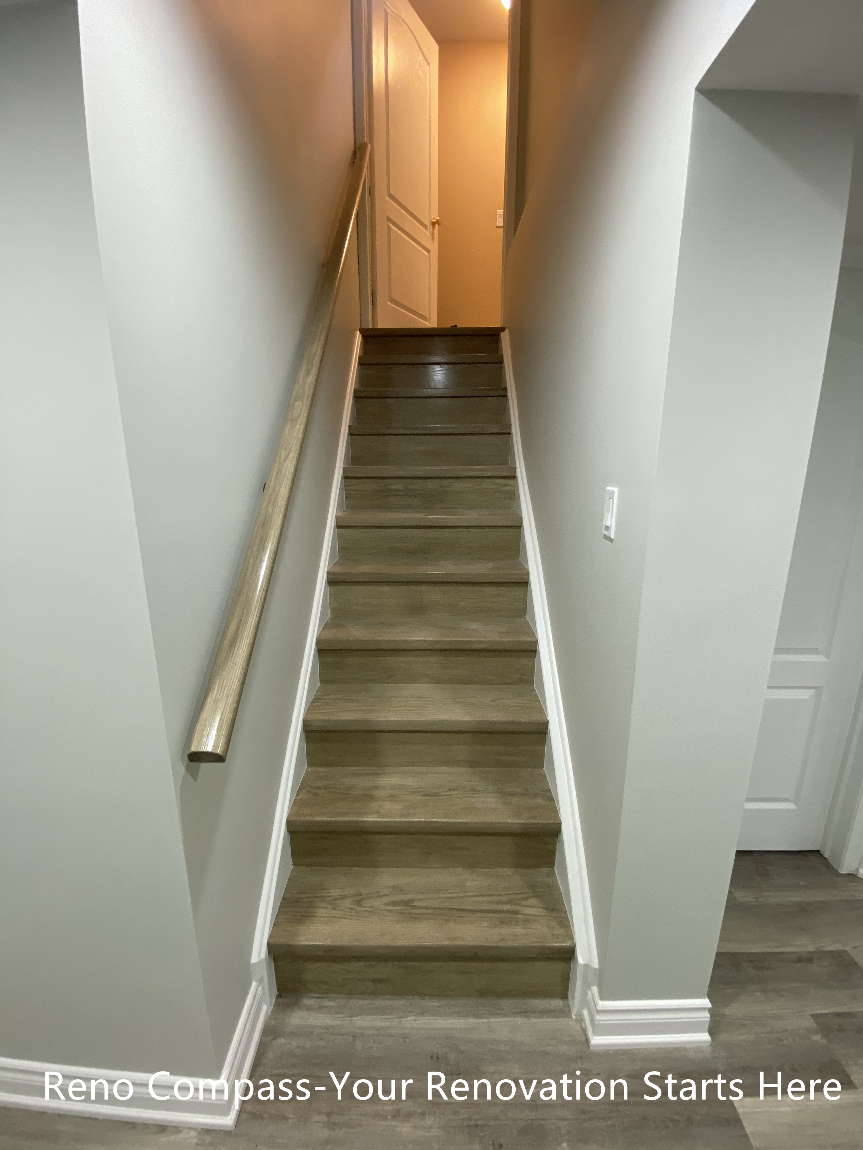 This image highlights the renovated basement staircase connecting the lower level to the main floor in this Aurora home. The staircase was refinished with durable, wood-look steps and clean white trim to create a cohesive transition between levels. Neutral wall colors and a streamlined handrail help keep the stairwell visually open while improving safety and everyday usability.

Recessed lighting was added above the stair opening to enhance visibility and reduce shadowing, making the space feel brighter and more inviting. By simplifying structural lines and finishes, the staircase integrates naturally into the overall basement layout without feeling enclosed or heavy. This renovation improves both circulation and visual continuity, supporting a clean, modern basement design.
City: Aurora | Toronto Contractor: Reno Compass