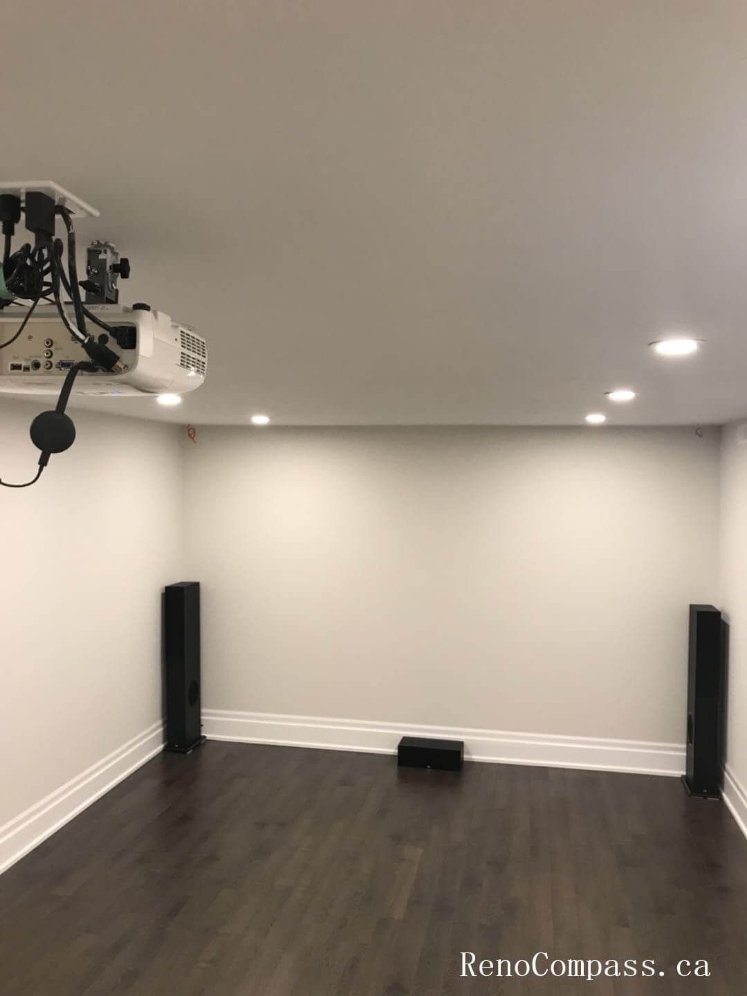 This image highlights a dedicated home theater area in a Richmond Hill basement renovation, featuring a ceiling‑mounted projector, recessed LED lighting, and dark hardwood flooring. The clean layout and integrated speaker setup create an ideal space for entertainment. Renovation completed by Reno Compass Inc.