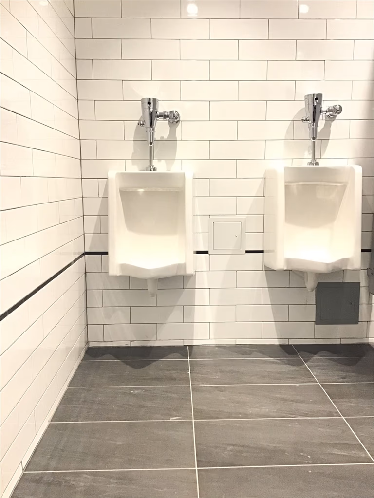 Commercial washroom renovation in downtown Toronto featuring wall-mounted urinals, white subway tile walls, and durable tile flooring, designed for functionality, hygiene, and high-traffic business environments.