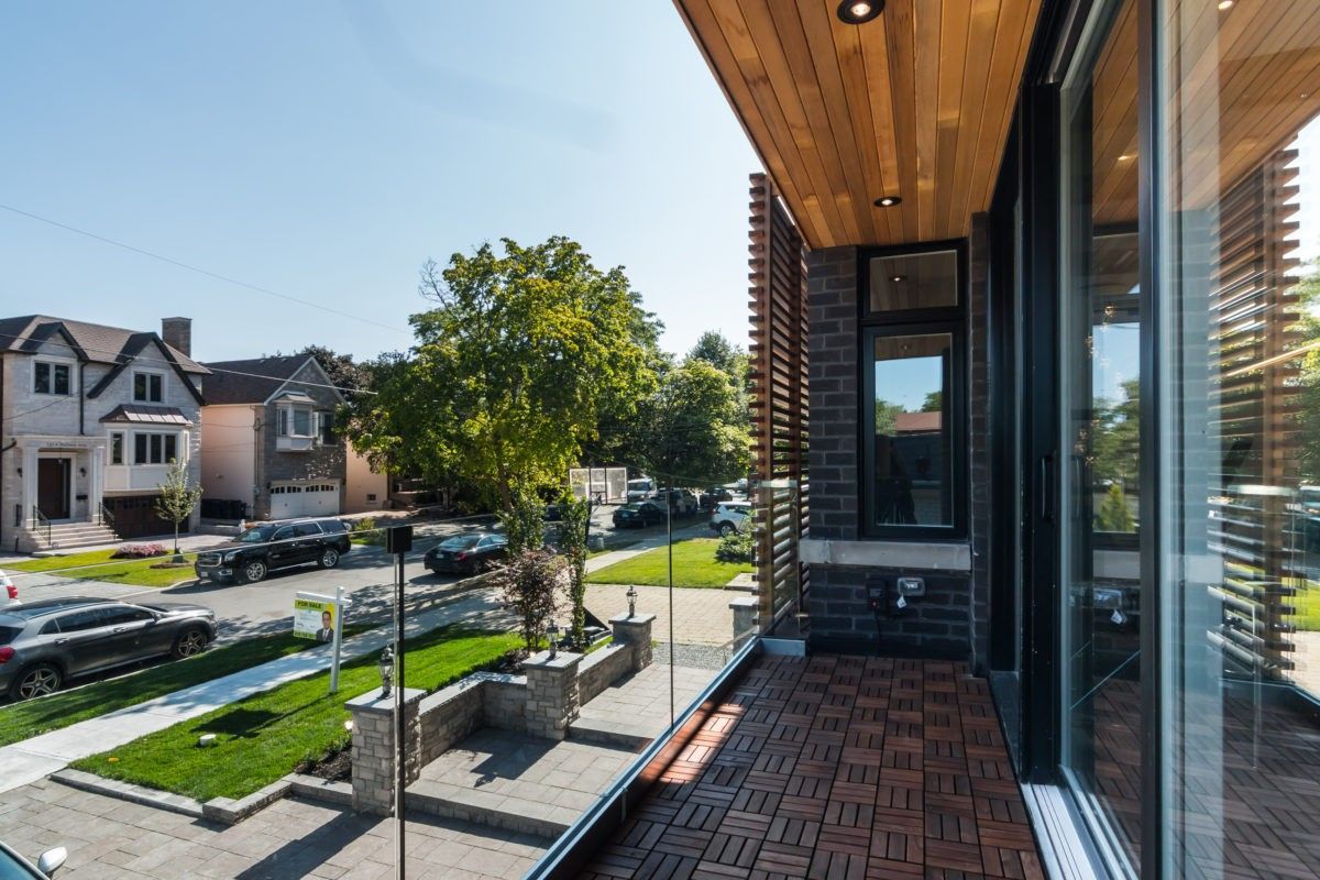 This Toronto modern-style home features a beautifully designed exterior balcony with sleek glass railings, warm wood ceiling panels, and contemporary brick finishes. The elevated front view enhances curb appeal while providing a functional outdoor space overlooking a landscaped front yard and residential street.