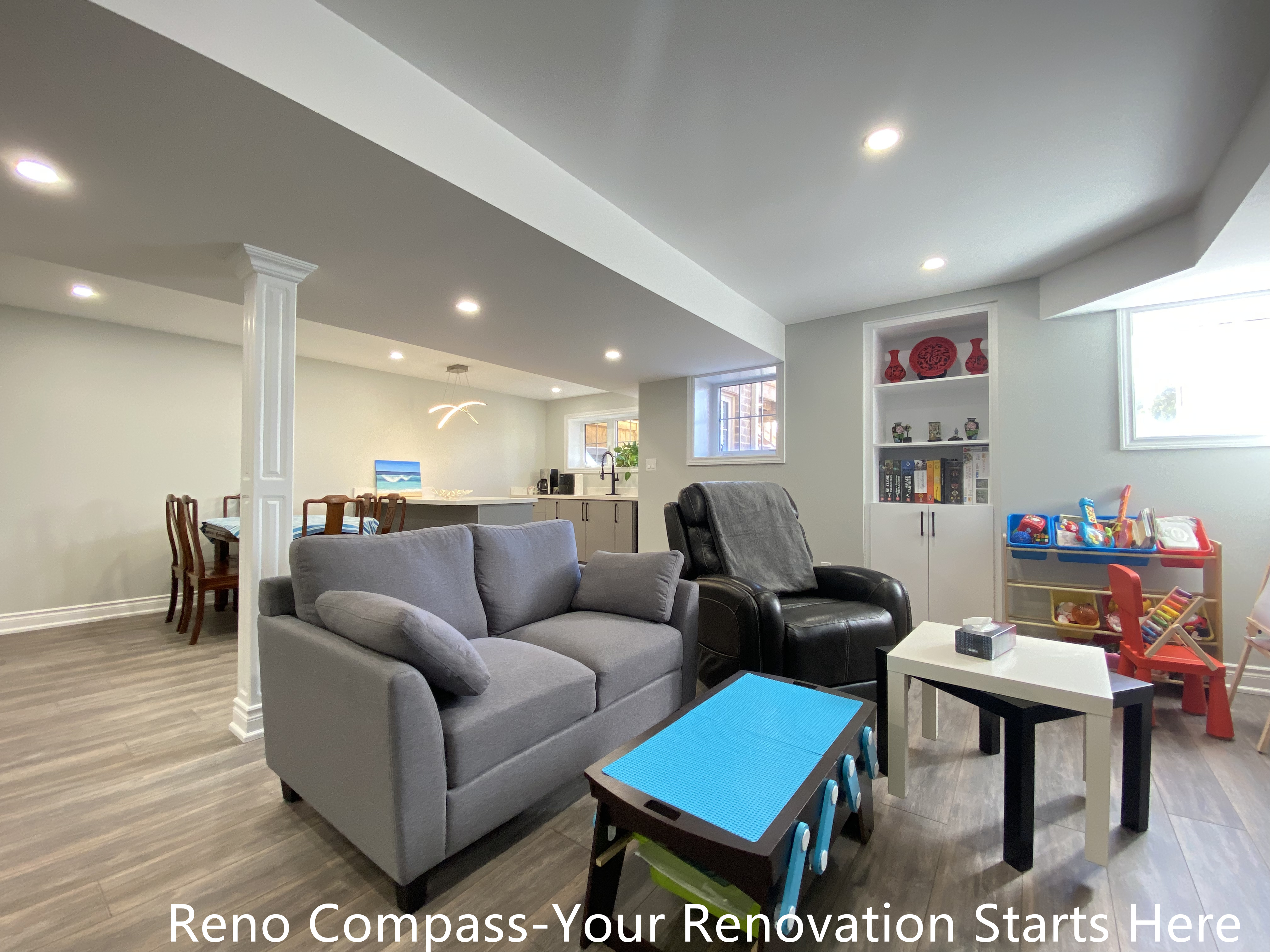 Modern open-concept basement renovation in Oakville featuring a bright family living area with vinyl flooring, recessed lighting, structural columns, custom built-in shelving, and a functional layout combining lounge, kids’ play area, and workspace, completed by Reno Compass Inc.