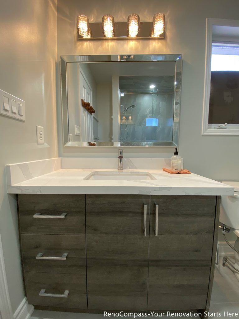 This Mississauga bathroom renovation features a modern vanity with wood-tone cabinetry, a clean white countertop, and a framed mirror paired with warm overhead lighting. The combination enhances both storage capacity and daily usability, while neutral wall colors keep the space bright and balanced.
City: Mississauga · Toronto contractor: Reno Compass