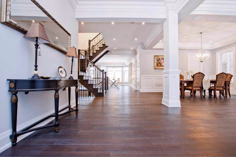 Elegant open-concept foyer and main living area completed through a Toronto design build custom build project. The interior features wide plank hardwood flooring, decorative columns, detailed ceiling moldings, and a custom staircase that connects the main floor layout. This whole house renovation Toronto project demonstrates high-end craftsmanship, thoughtful spatial planning, and the seamless integration of dining and living areas typical of luxury custom build homes in Toronto.