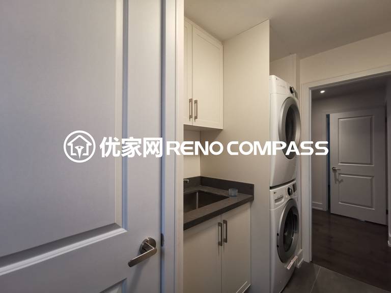This image showcases a custom-designed laundry room completed as part of a North York interior renovation project. The space features a stacked washer and dryer setup, maximizing vertical storage while maintaining a clean and modern layout. Custom white cabinetry provides ample storage, paired with a dark quartz countertop and integrated sink for practical daily use. The compact yet efficient design reflects thoughtful space planning and high-quality craftsmanship, making it ideal for modern Toronto homes seeking functional interior upgrades.