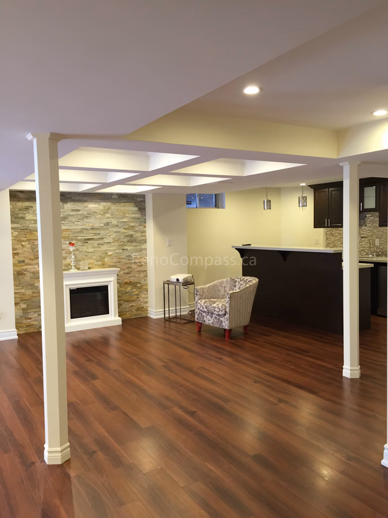 This Toronto basement renovation features a modern open-concept layout with rich hardwood flooring, custom ceiling beam design, recessed lighting, and a stylish stone accent wall with fireplace. Completed by Reno Compass Inc., this upgraded basement offers a warm and functional living space perfect for entertainment and relaxation, enhancing both comfort and property value.