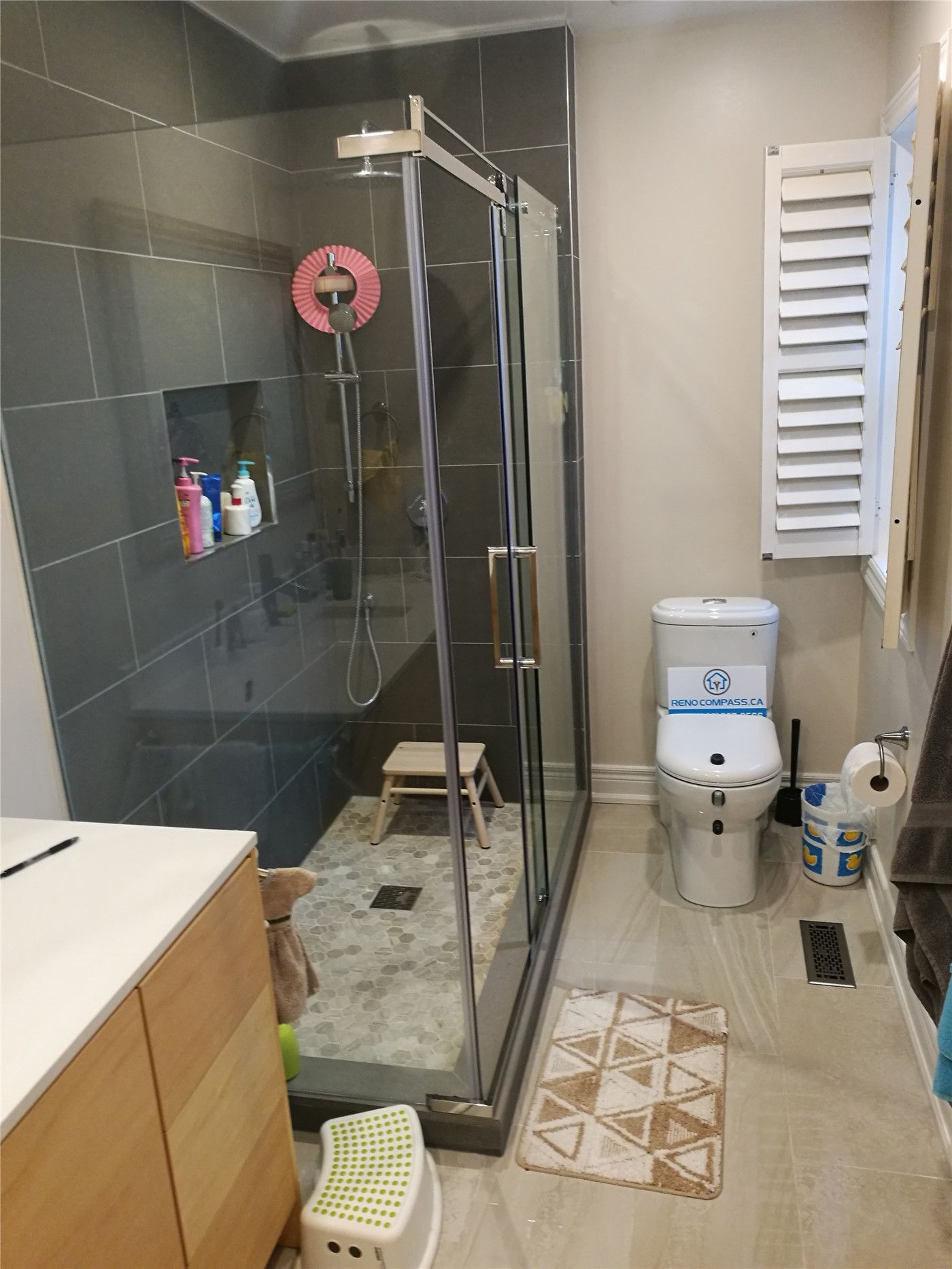 This Richmond Hill bathroom renovation features a modern glass walk-in shower with dark large-format wall tiles, built-in storage niche, and a sleek chrome shower system. The spacious layout, slip-resistant shower flooring, and contemporary vanity create a functional and stylish bathroom upgrade. Completed by a professional Toronto renovation company, this project highlights quality craftsmanship, efficient space planning, and durable materials designed for everyday comfort and long-term performance.