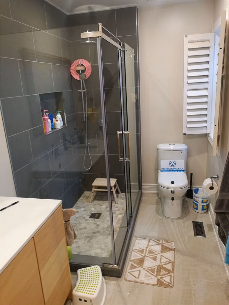 This Richmond Hill bathroom renovation features a modern glass walk-in shower with dark large-format wall tiles, built-in storage niche, and a sleek chrome shower system. The spacious layout, slip-resistant shower flooring, and contemporary vanity create a functional and stylish bathroom upgrade. Completed by a professional Toronto renovation company, this project highlights quality craftsmanship, efficient space planning, and durable materials designed for everyday comfort and long-term performance.