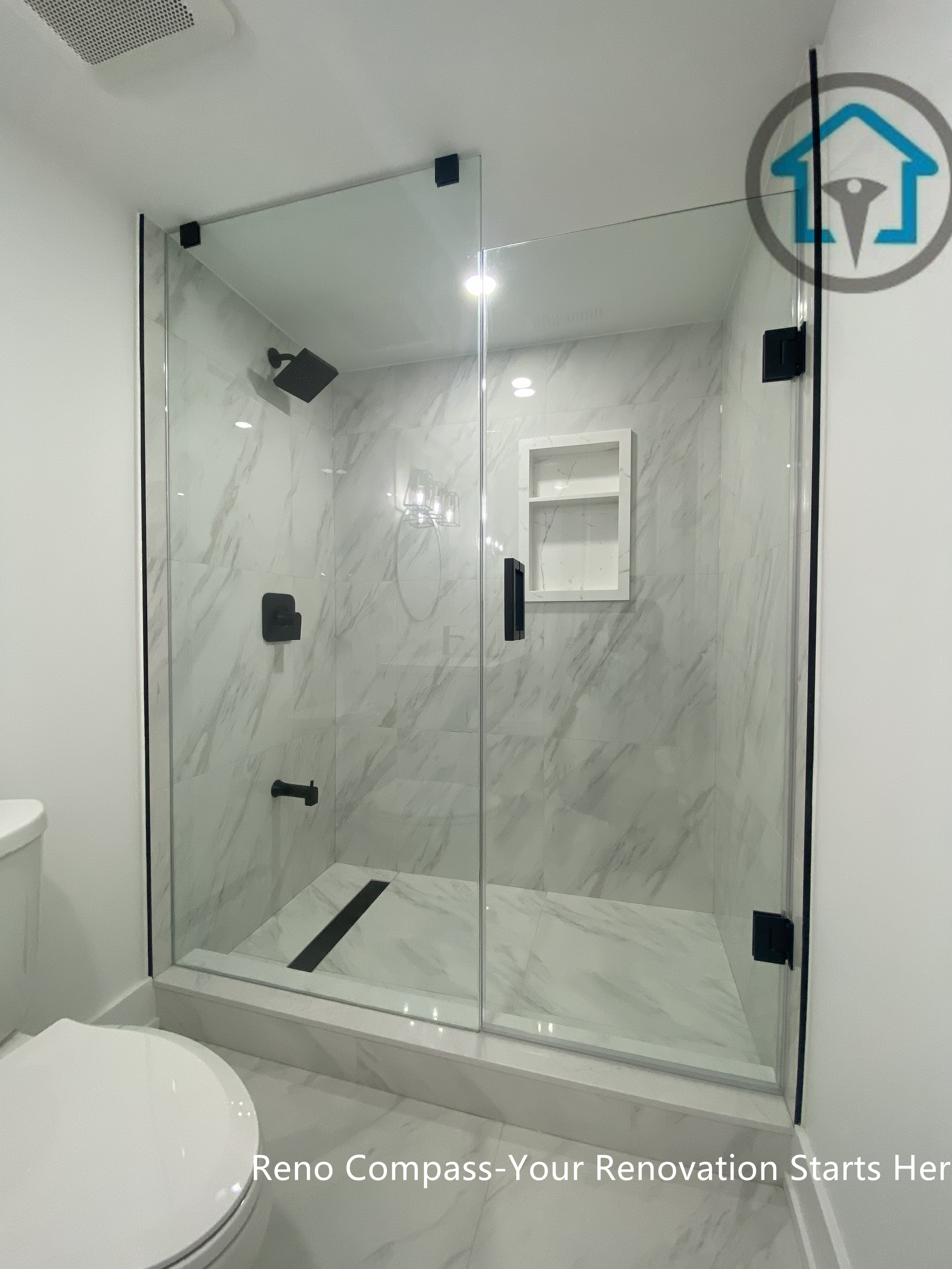 This image showcases a modern basement bathroom renovation in Newmarket completed by a professional Toronto renovation company. The walk-in shower features full-height marble-look tiles, a frameless glass enclosure with black hardware, built-in niche shelving, and a linear floor drain. Clean white finishes and contemporary fixtures create a bright, low-maintenance, and functional basement bathroom ideal for rental units or family use.