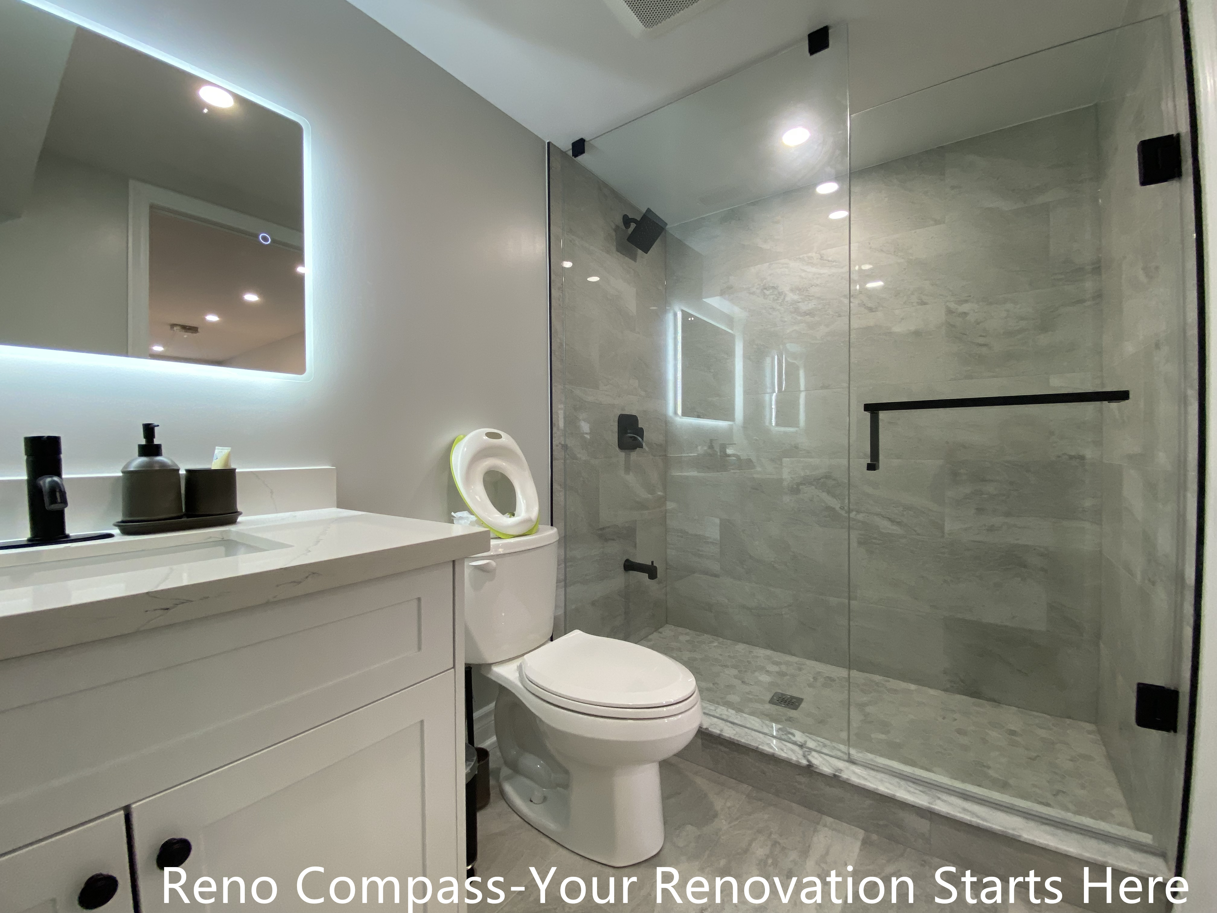 Modern basement bathroom renovation in Oakville featuring a walk-in glass shower with marble-look tiles, frameless glass enclosure, matte black fixtures, custom vanity with quartz countertop, and a clean, functional layout designed for everyday use, completed by Reno Compass Inc.