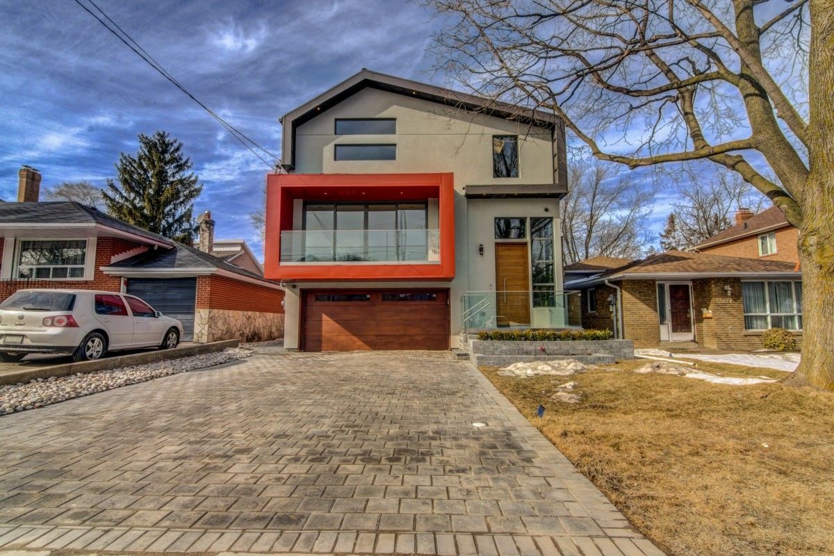 Modern custom home exterior in Toronto featuring a bold contemporary facade, large windows, second-floor balcony, and wide interlocking stone driveway. The design combines clean architectural lines with warm wood and stone accents, creating strong curb appeal and modern luxury living. Completed by a professional Toronto renovation company, this exterior renovation highlights high-end residential design and quality craftsmanship.