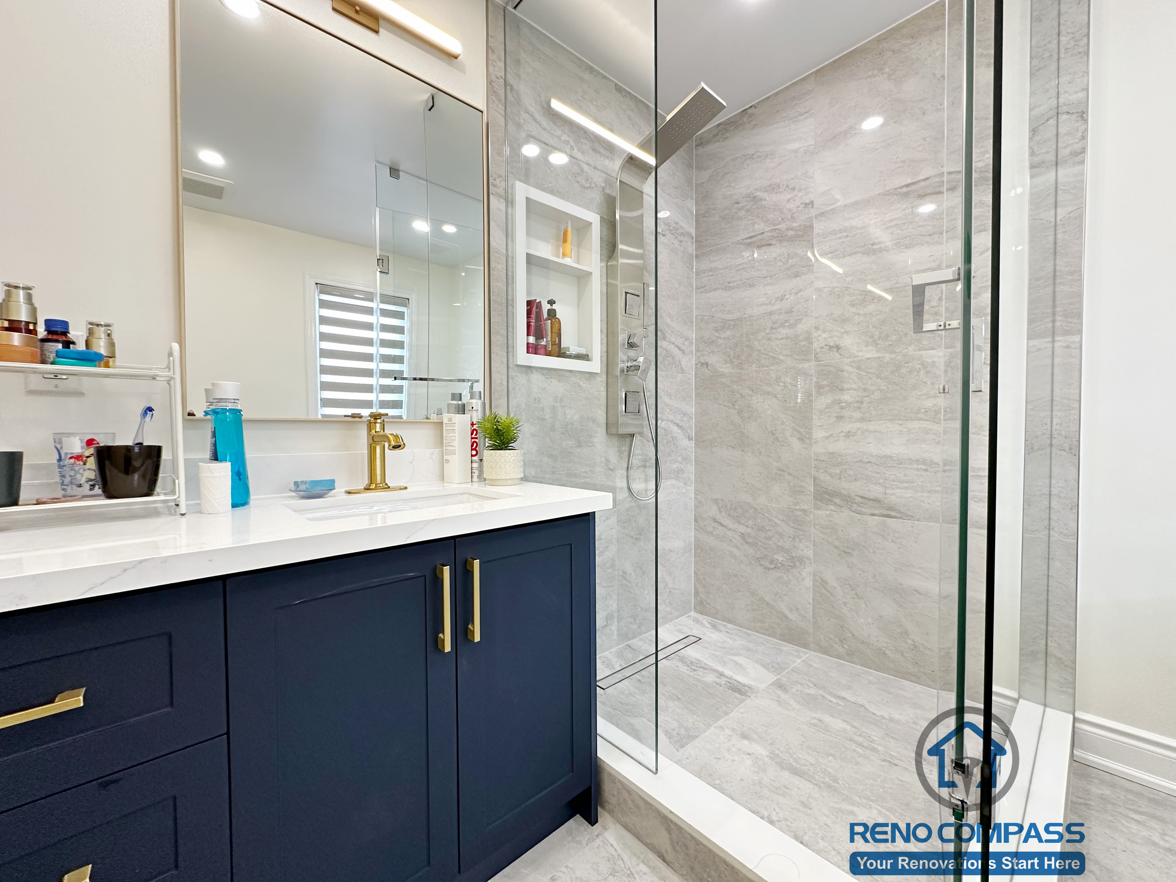 Master bathroom renovation in Markham featuring a custom navy vanity with quartz countertop, brass fixtures, and a walk-in glass shower with large-format tile. The design emphasizes clean detailing, durability, and a modern spa-like atmosphere.