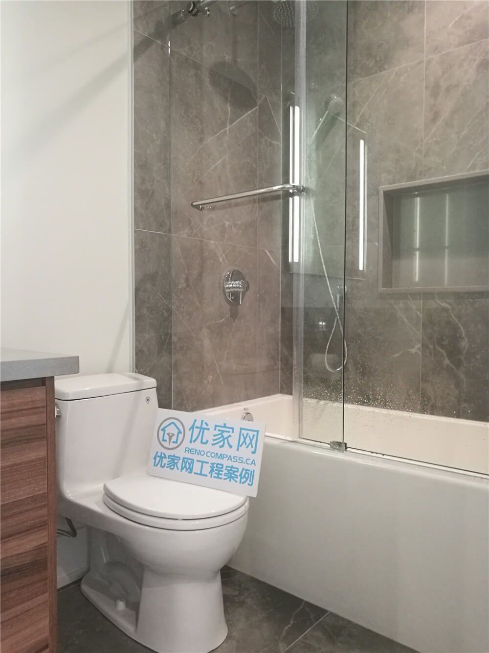 This North York interior renovation features a modern bathroom with a glass tub enclosure, large-format stone-look wall tiles, and a clean, functional layout. The design emphasizes easy maintenance, moisture protection, and a neutral aesthetic suitable for everyday family use.
