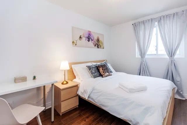 This Toronto interior renovation features a bright and cozy bedroom with clean white walls, minimalist furniture, and soft decorative accents. The space includes a comfortable bed, modern bedside lighting, and simple artwork that enhances the calm atmosphere. The renovation creates a relaxing and functional bedroom environment, perfect for comfortable living in a modern Toronto home.