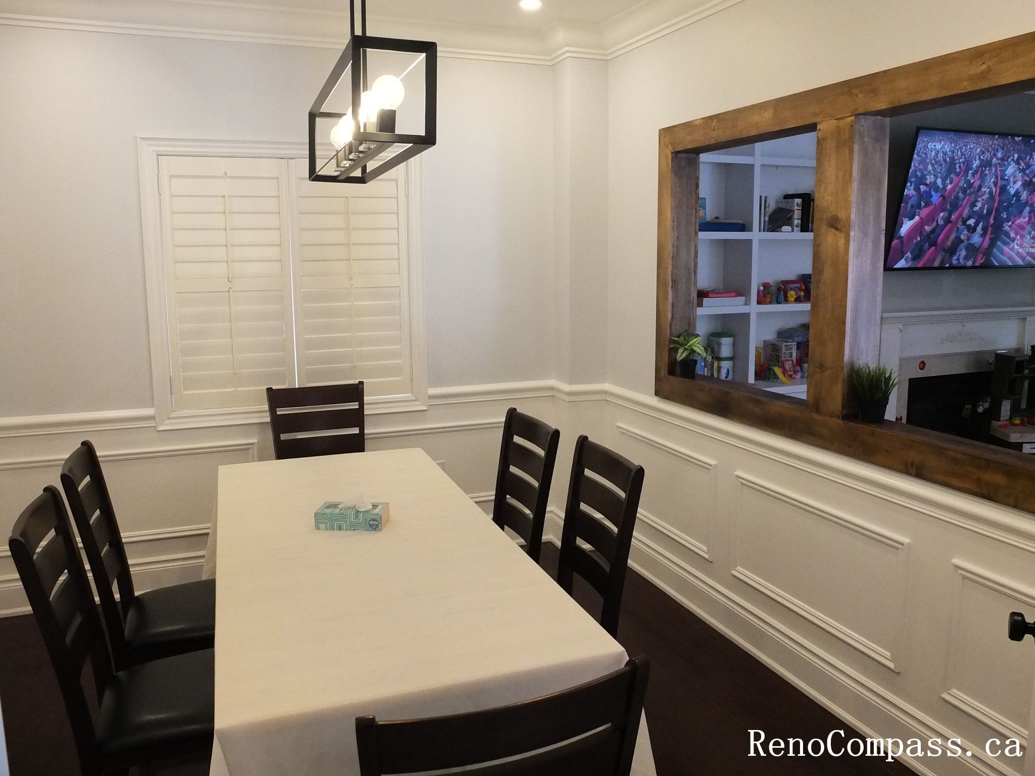 This Newmarket interior renovation features a clean and elegant dining room designed with classic wall wainscoting and rich dark hardwood flooring. Plantation shutters allow natural light to brighten the space while maintaining privacy, and the modern rectangular pendant light provides balanced illumination above the dining table. The simple layout and refined finishes create a comfortable setting for family meals and gatherings. Completed by Reno Compass Inc., this project highlights timeless interior design and high-quality craftsmanship for modern homes.