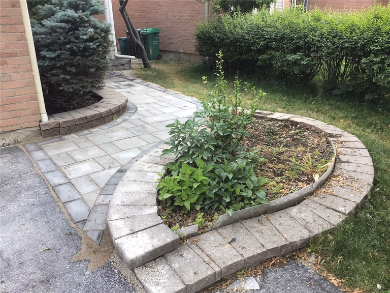 This Oakville interlocking project features a beautifully curved walkway integrated with a raised garden bed and natural stone borders. The soft curve design enhances the landscape flow while maintaining a clean and structured layout. Built with durable grey pavers, this installation improves accessibility, drainage, and curb appeal, creating a harmonious blend between hardscape and greenery.