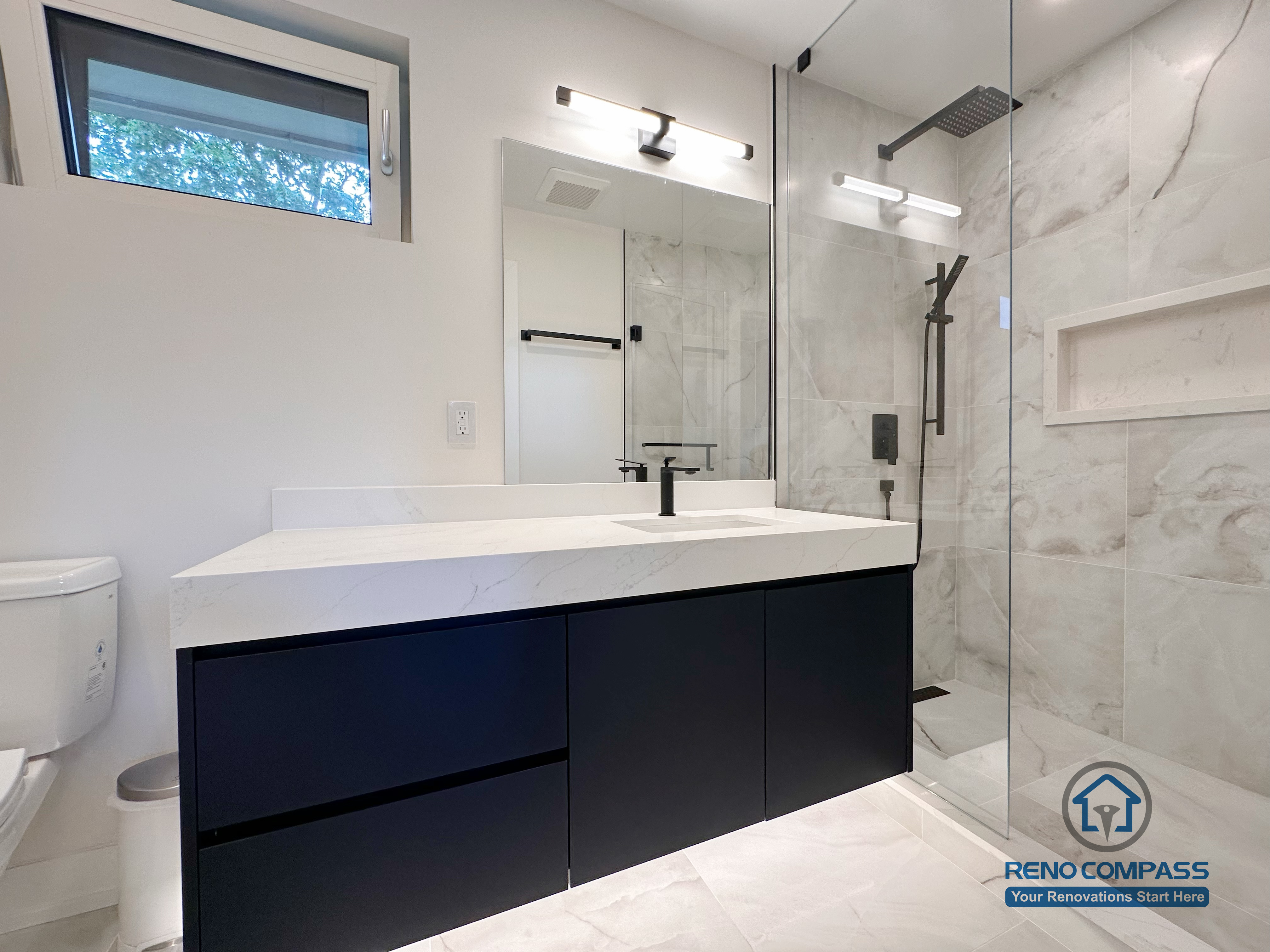 Contemporary bathroom renovation in Toronto featuring a custom floating vanity, integrated sink, frameless walk-in glass shower, built-in wall niche, matte black fixtures, and marble-look porcelain tile walls. Completed by a trusted Toronto renovation company with attention to space efficiency and modern design.