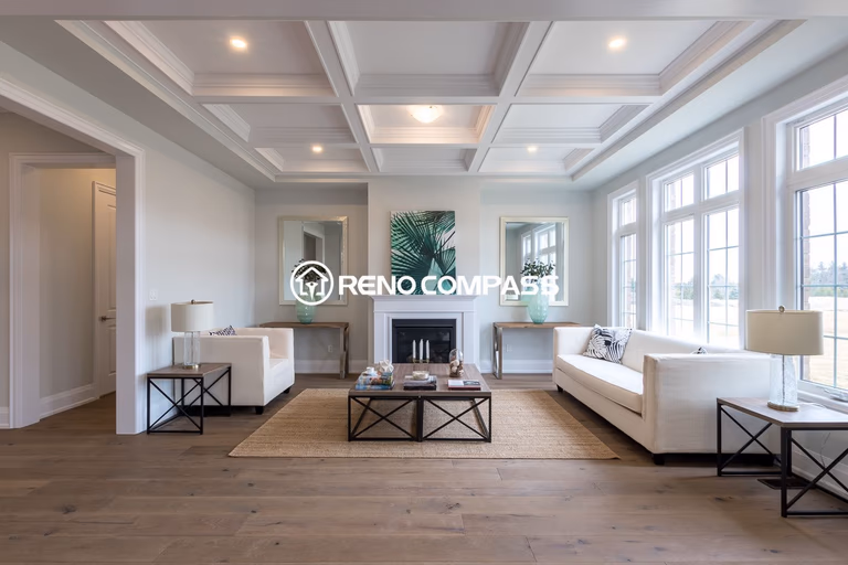 Beautiful living room renovation in Newmarket featuring a coffered ceiling design, large windows for natural light, and engineered hardwood flooring. The elegant layout with modern furniture and a central fireplace creates a bright and sophisticated open-concept living space connected to the kitchen area.