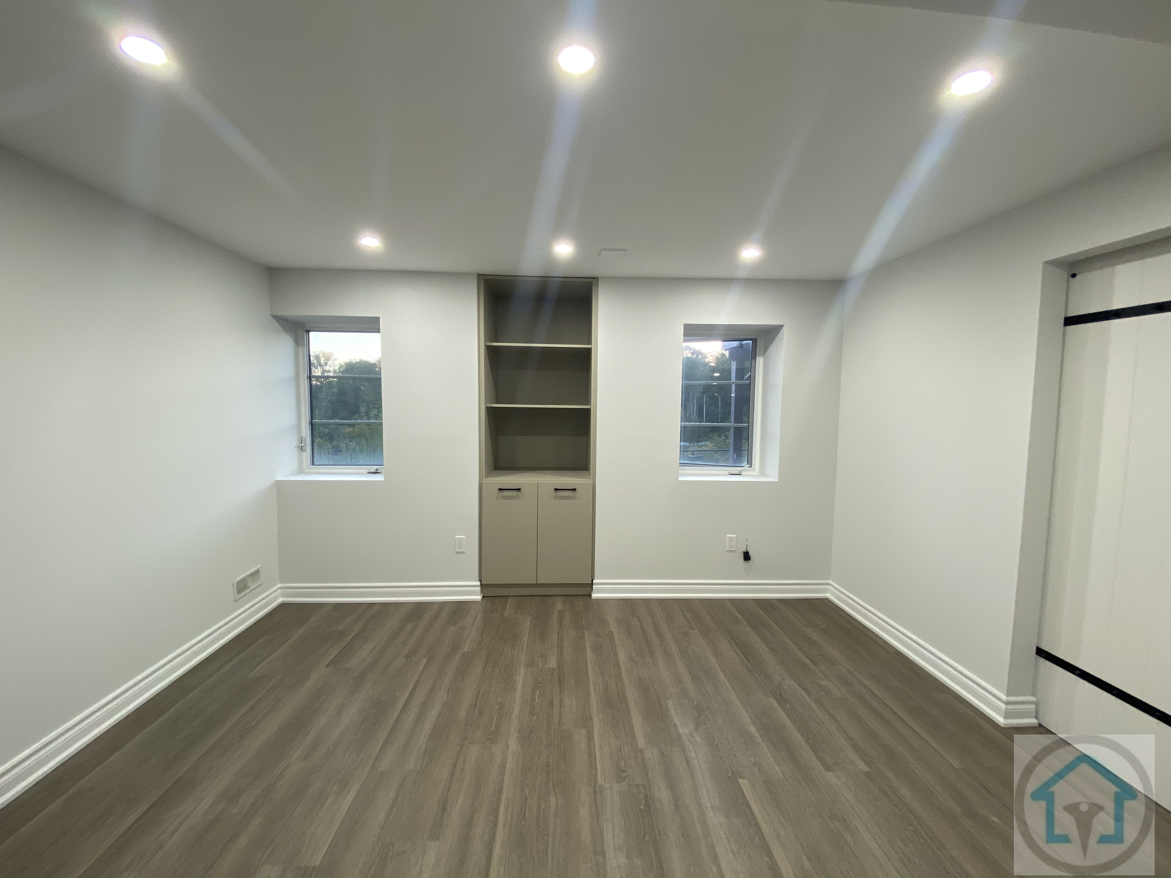Bright and modern Aurora basement space featuring two windows for natural light, built-in shelving for storage, and sleek flooring, ideal for a bedroom, office, or flexible living area. Contractor: Reno Compass Inc.
