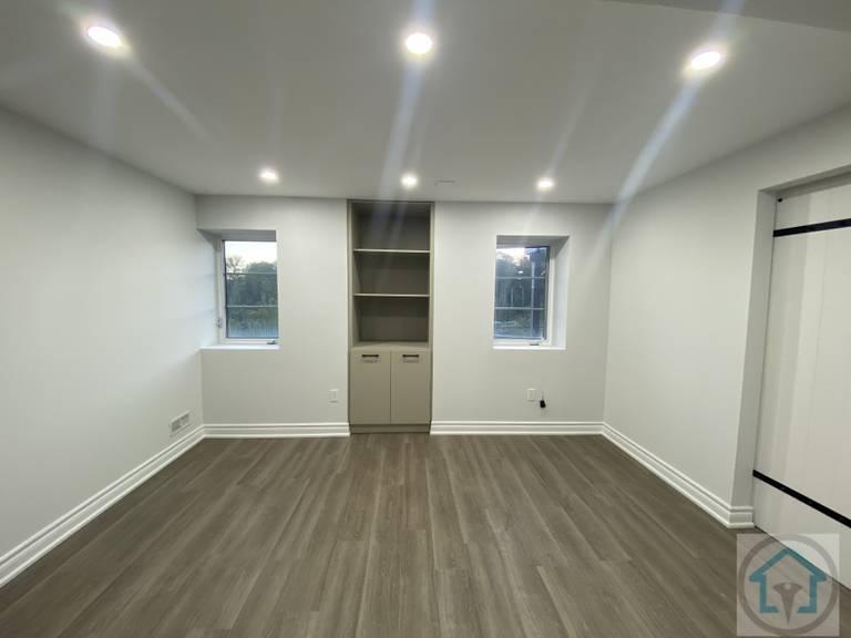 Bright and modern Aurora basement space featuring two windows for natural light, built-in shelving for storage, and sleek flooring, ideal for a bedroom, office, or flexible living area. Contractor: Reno Compass Inc.