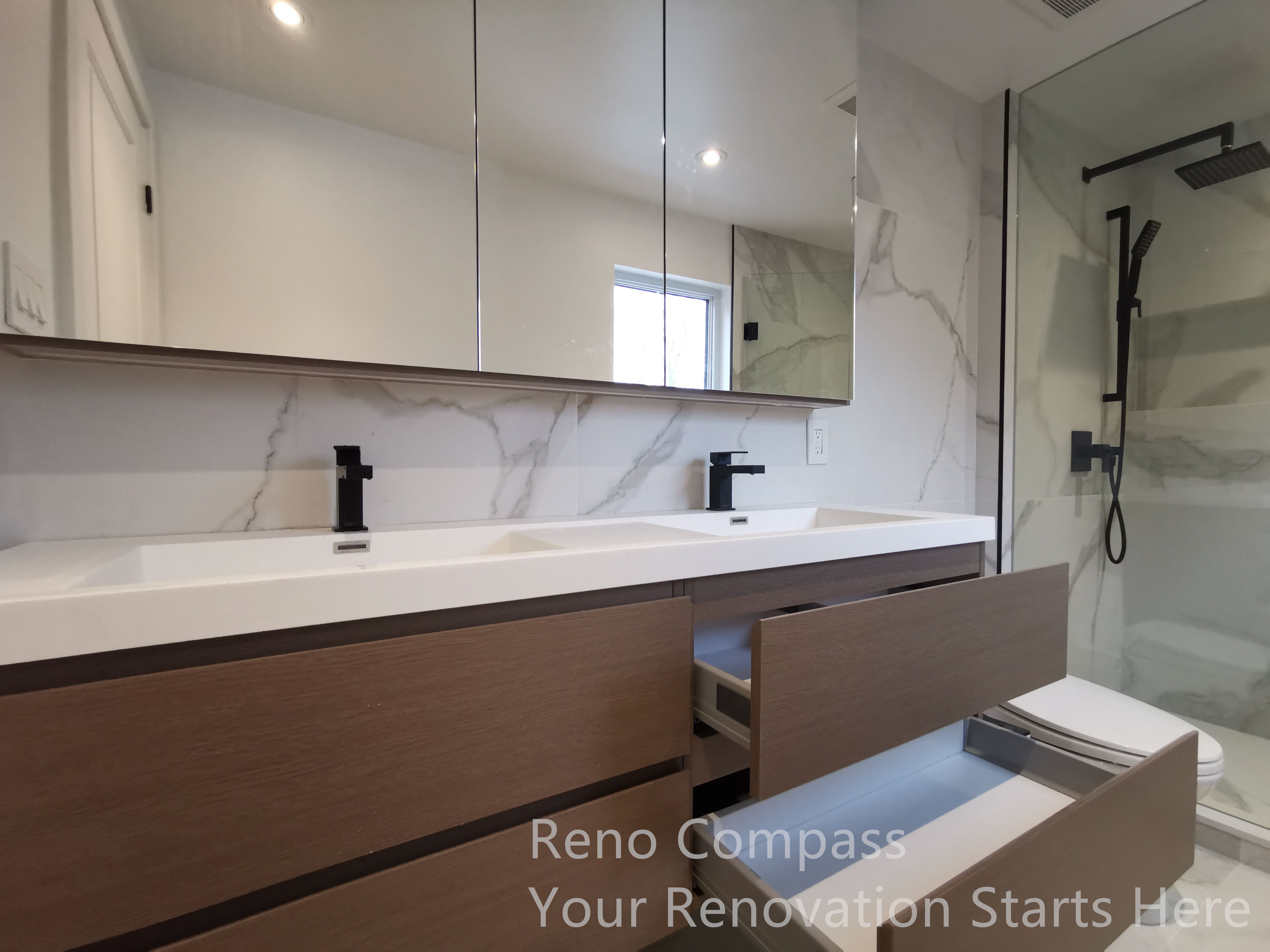 This image highlights a custom double vanity completed as part of a Markham interior renovation. Warm wood-tone cabinetry is paired with a clean white countertop, creating a balanced contrast between modern minimalism and natural texture. The handle-less drawers offer generous storage while maintaining a streamlined appearance, and the integrated mirror cabinets enhance both functionality and visual depth. Matte black faucets add a refined, contemporary accent, completing a bathroom design focused on daily comfort, durability, and long-term usability.