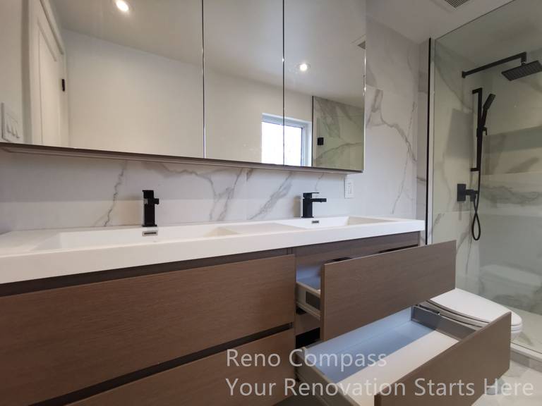 This image highlights a custom double vanity completed as part of a Markham interior renovation. Warm wood-tone cabinetry is paired with a clean white countertop, creating a balanced contrast between modern minimalism and natural texture. The handle-less drawers offer generous storage while maintaining a streamlined appearance, and the integrated mirror cabinets enhance both functionality and visual depth. Matte black faucets add a refined, contemporary accent, completing a bathroom design focused on daily comfort, durability, and long-term usability.
