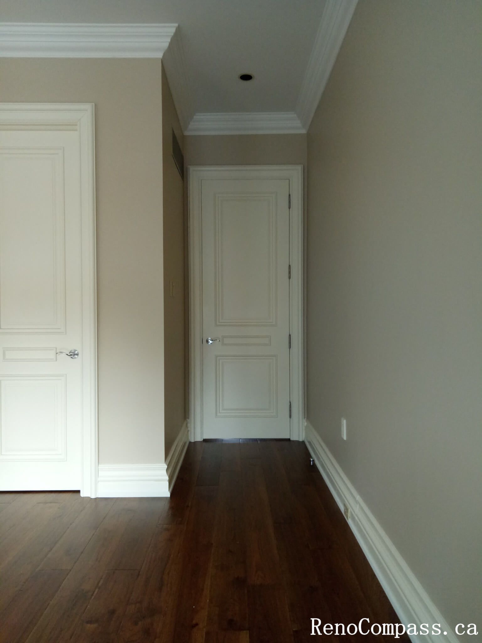 This image presents a completed interior painting project in North York, showcasing a clean hallway space with freshly painted walls, detailed door trim, and crisp crown molding. The soft neutral wall color enhances the depth of the corridor while complementing the white doors and trim for a refined, cohesive look. Smooth transitions between walls, ceilings, and baseboards highlight careful preparation and professional application. This North York painting project reflects high-quality craftsmanship, creating a bright and elegant interior finish suitable for hallways and connecting spaces.